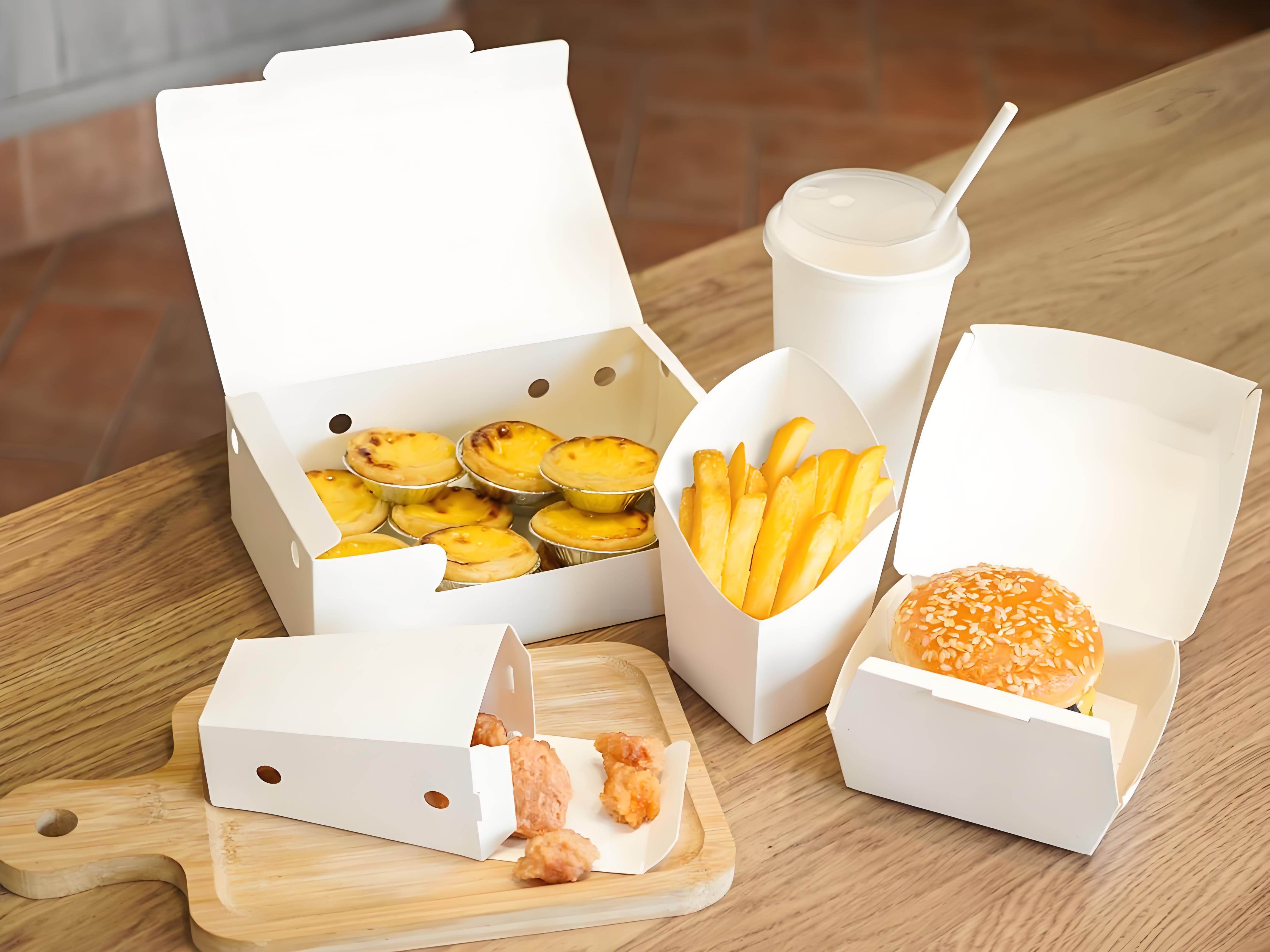 Food-grade paper packaging set with burger boxes, fry scoops, tart boxes and paper cups on a wooden table
