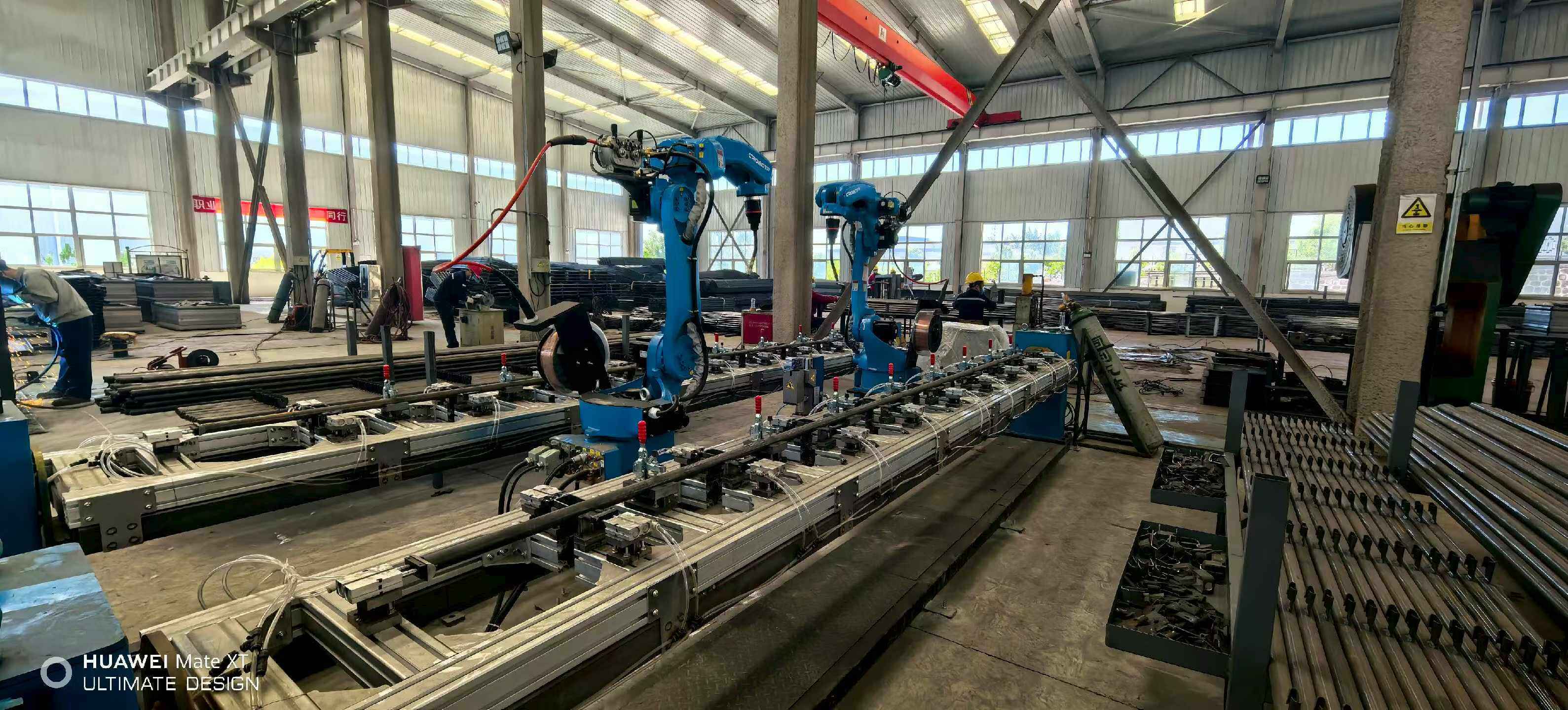 Blue robotic welding arms working on cage frames along the production line