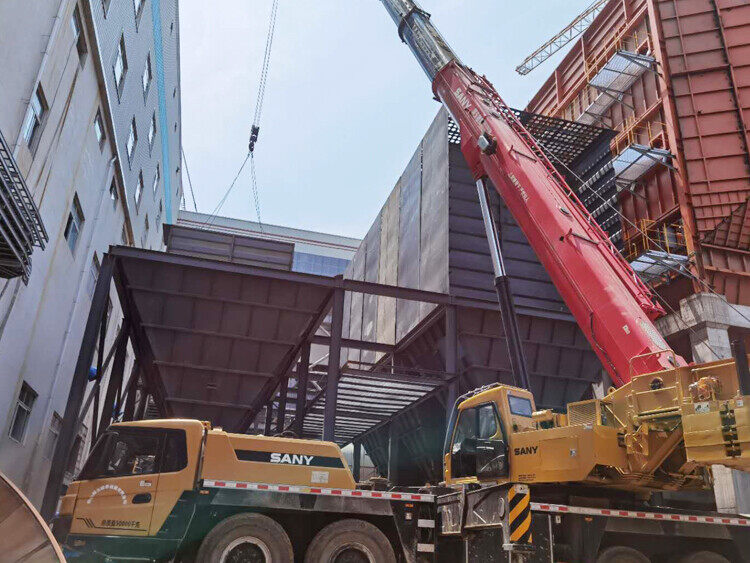 Mobile crane lifting a large steel hopper module beside the plant building during on-site installation