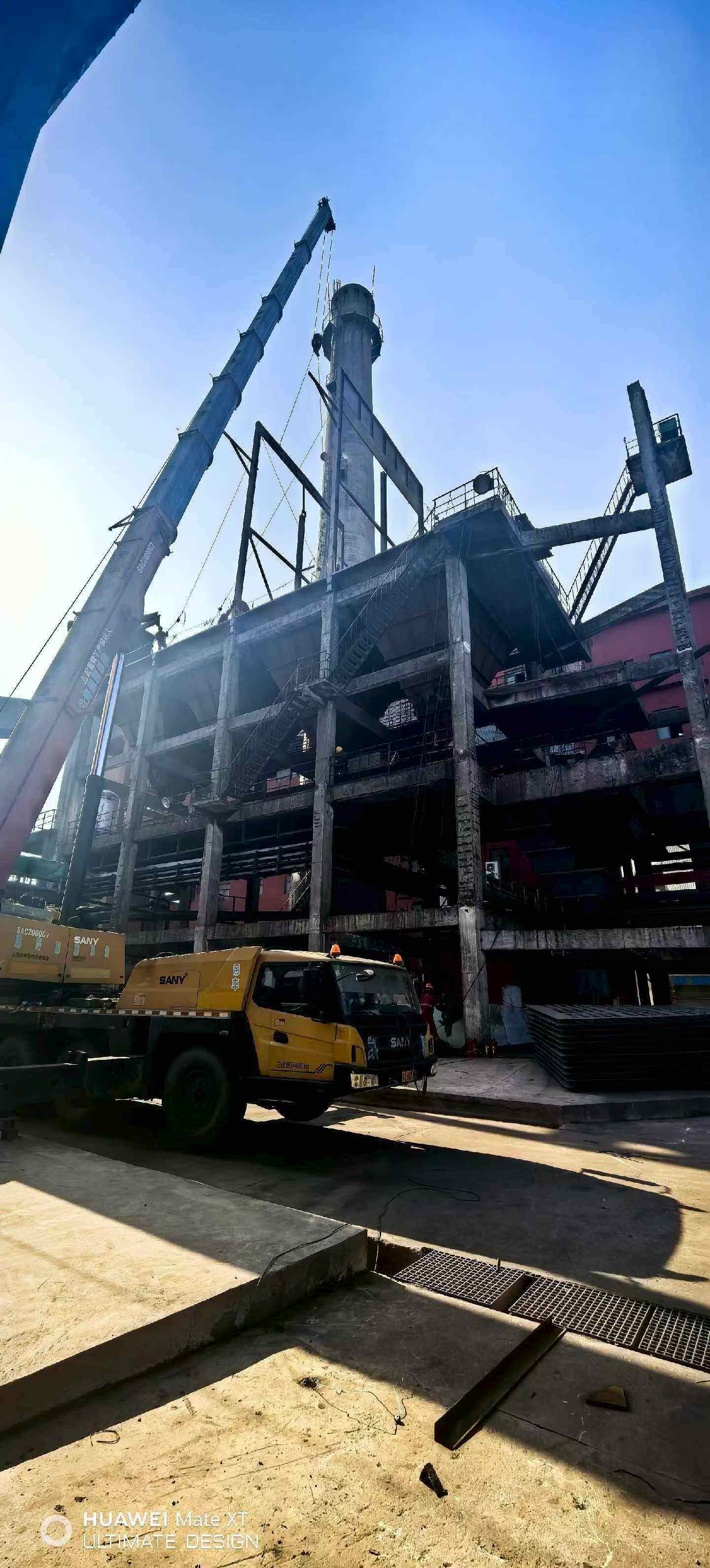 Mobile crane erecting steel support frames beside a concrete stack and multi-storey collector structure
