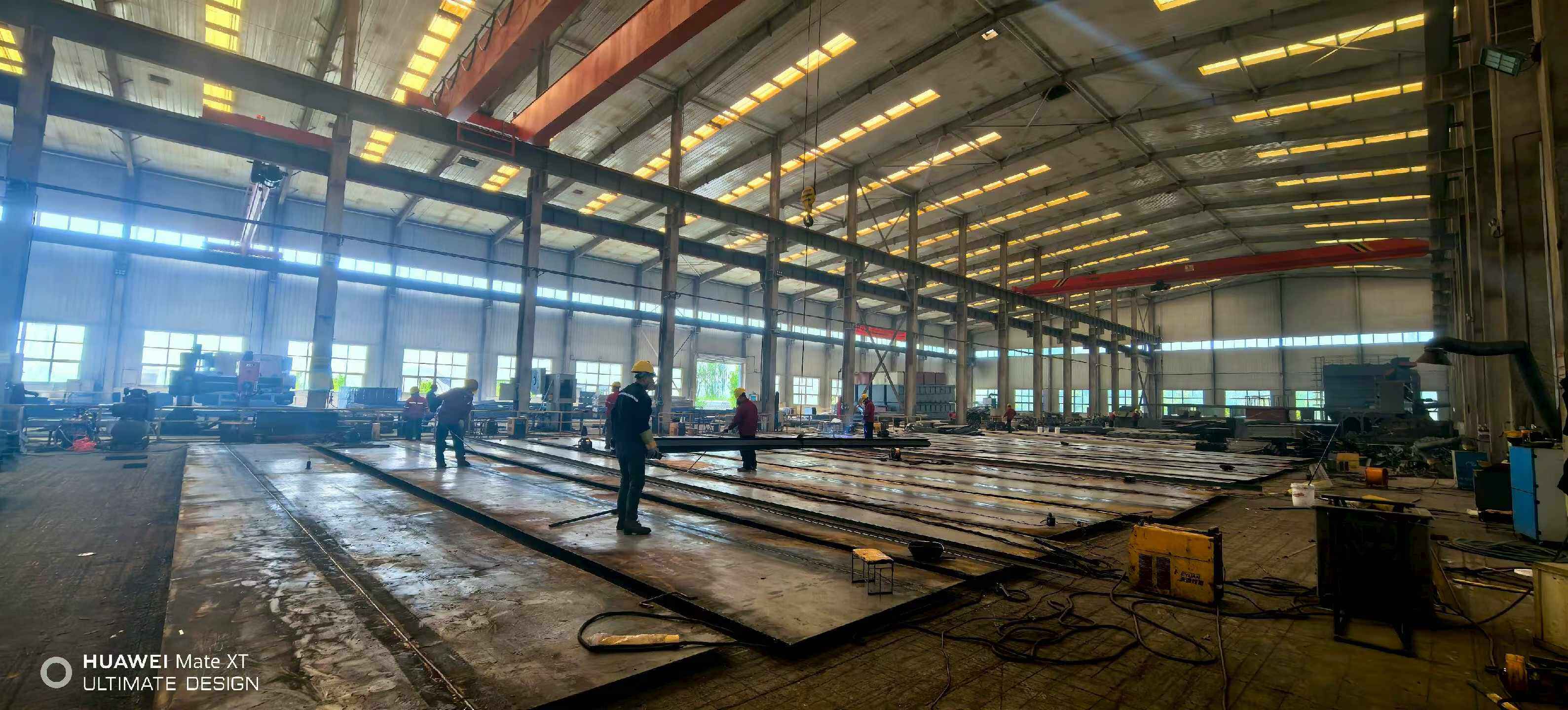 Workers laying out and marking long steel plates on the workshop floor