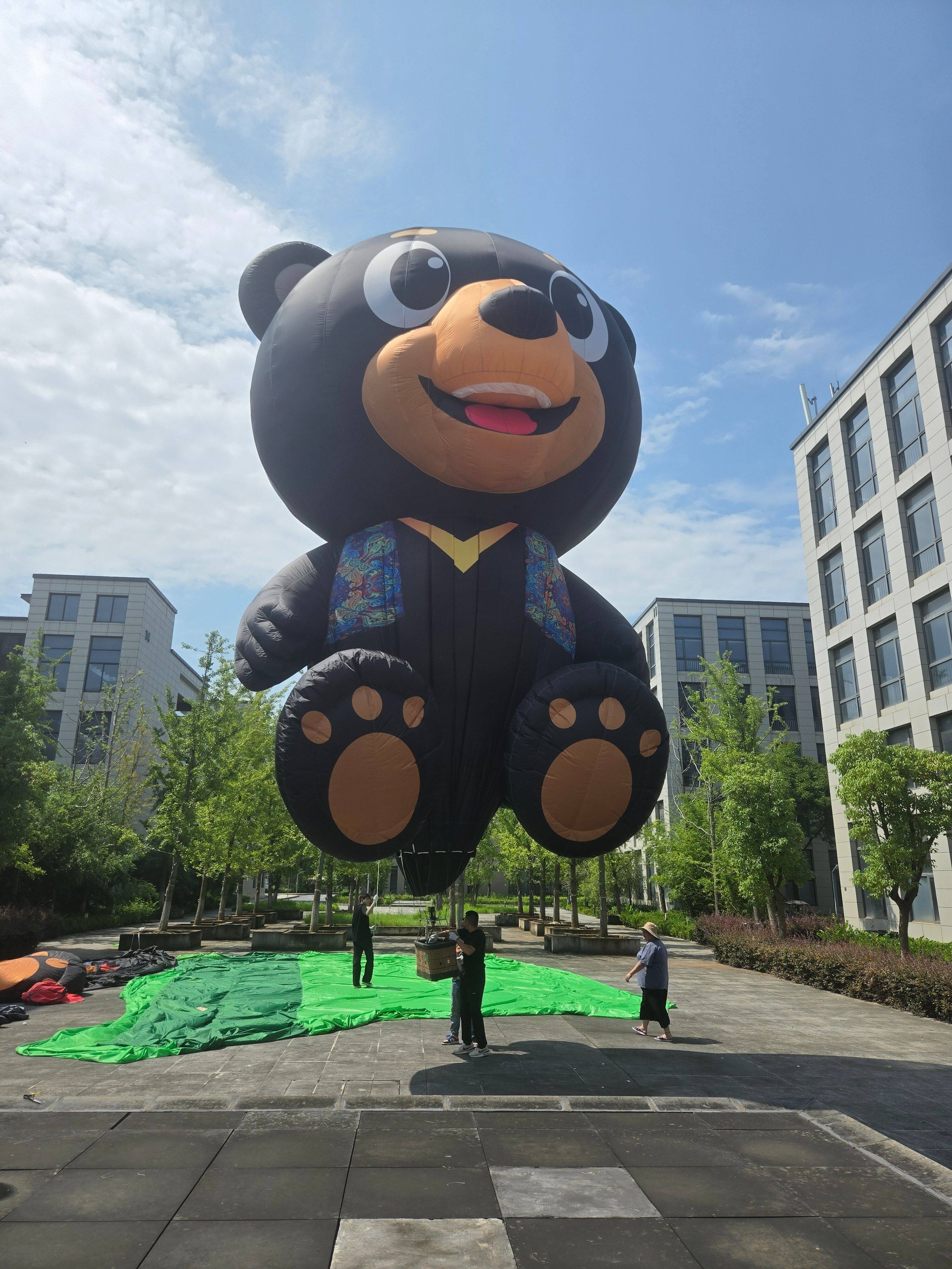 Side view of a black cartoon bear-shaped remote-controlled hot air balloon. Features a black body, brown paws, and a colorful scarf for a cute, high-recognizability design. Ideal for scenic attractions, brand collaborations, and outdoor displays.