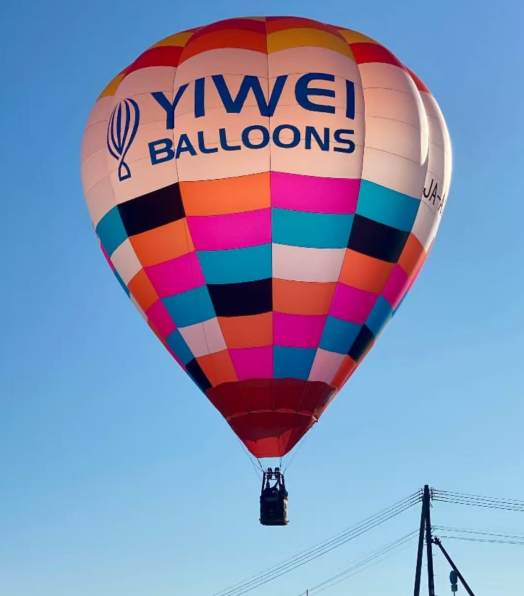 Yiwei Balloons Branded Multi-Color Checkered Hot Air Balloon - Manned Hot-Air Balloons by Yiwei Balloons - Yiwei Balloons branded multi-color checkered manned hot air balloon flying in clear blue sky with wicker basket.