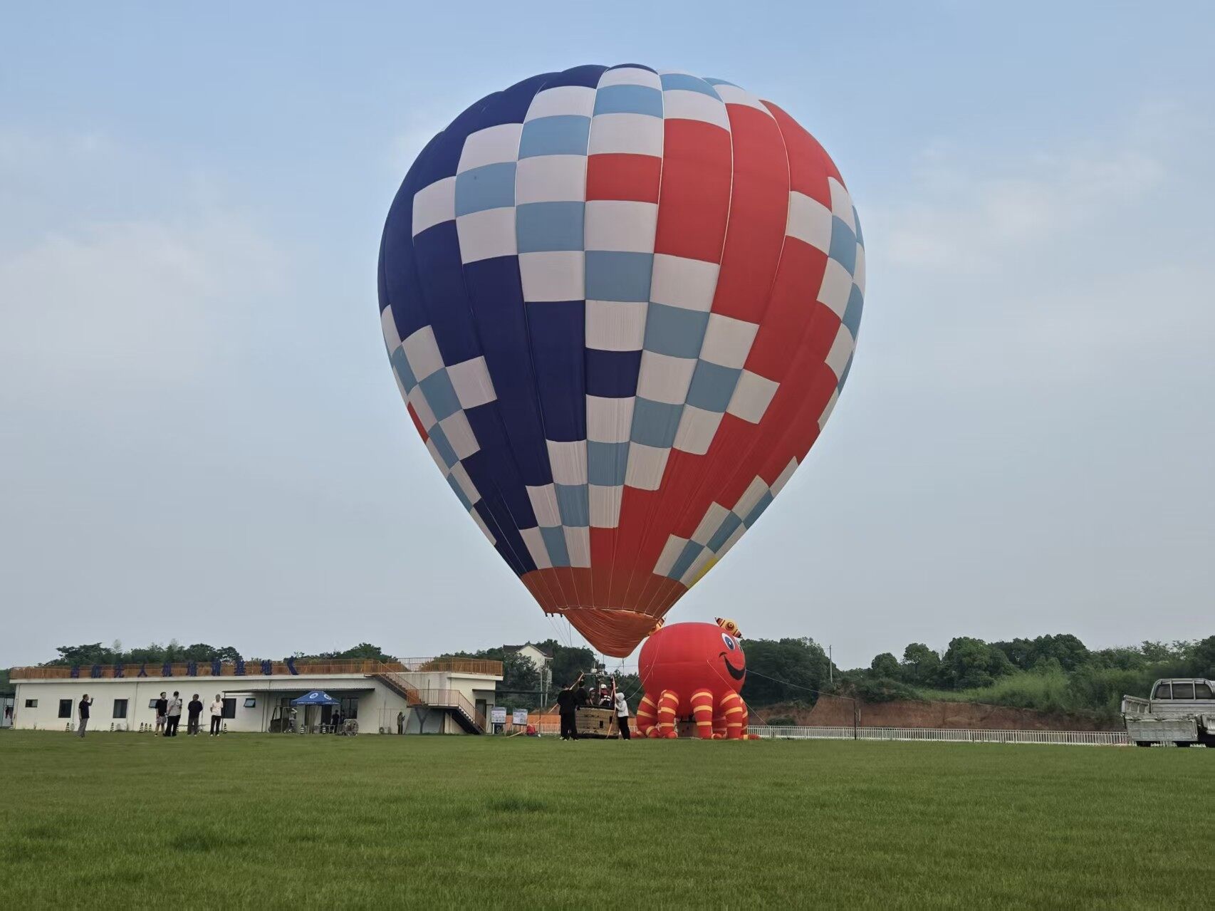Red Blue White Checkered Manned Hot Air Balloon with Inflatable Crab - Manned Hot-Air Balloons by Yiwei Balloons - Red blue and white checkered manned hot air balloon with inflatable crab mascot at outdoor event on grass field.