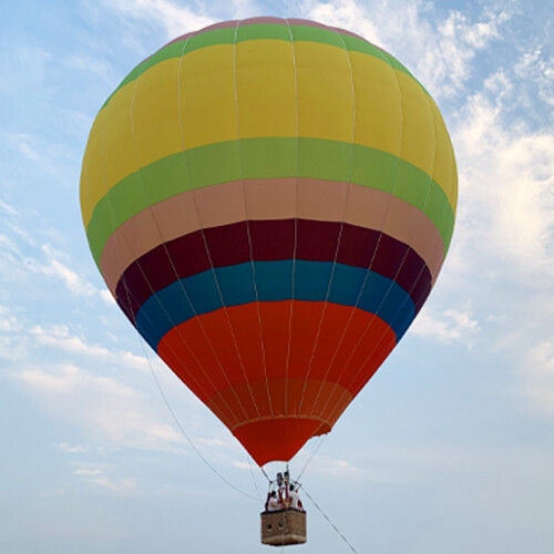 Yellow Green Red Striped Manned Hot Air Balloon in Flight - Manned Hot-Air Balloons by Yiwei Balloons - Yellow green and red striped manned hot air balloon flying against blue sky with wicker basket carrying passengers.