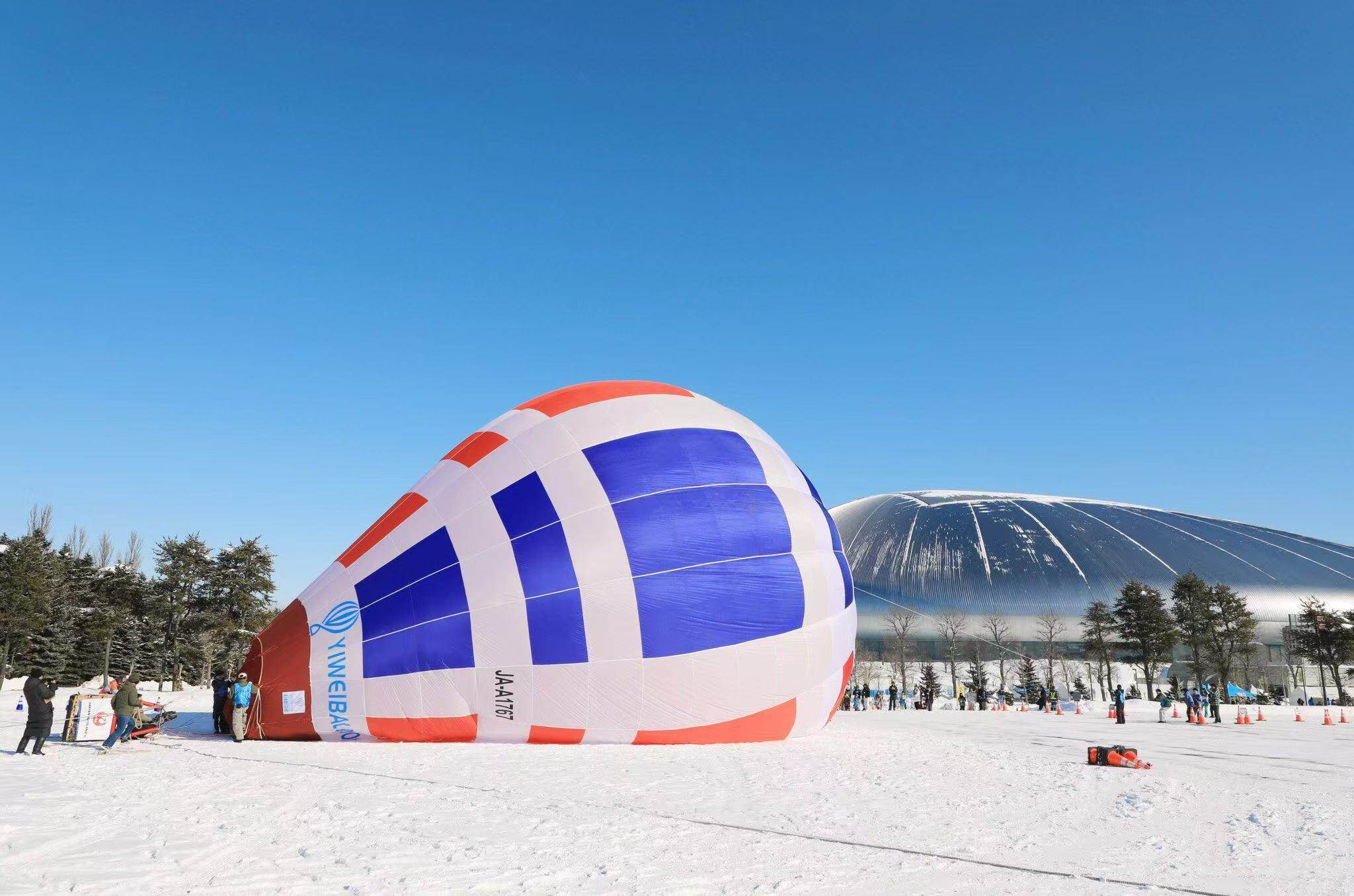 Red White Blue Manned Hot Air Balloon in Snow - Manned Hot-Air Balloons by Yiwei Balloons - Red white and blue manned hot air balloon being inflated in snowy landscape with dome building background in Japan.