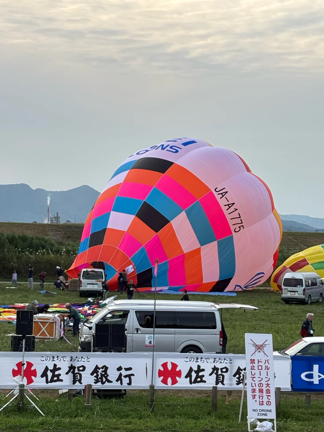 Yiwei Balloons at Saga International Balloon Fiesta Japan Yiwei Balloons hot air balloon at Saga International Balloon Fiesta in Japan - colorful balloon JA-A1775 being inflated on grass field with Saga Bank banner
