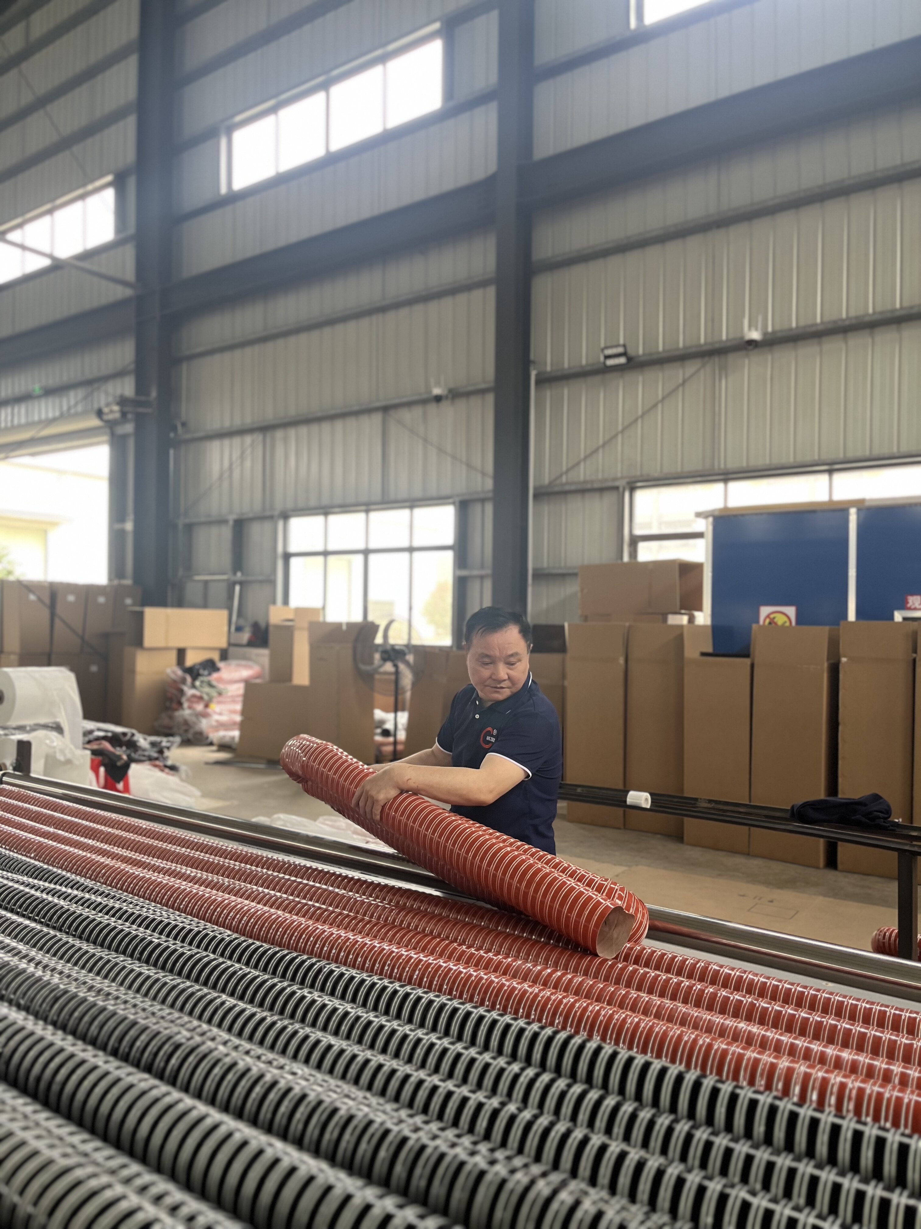 Worker handling flexible duct hoses in factory warehouse