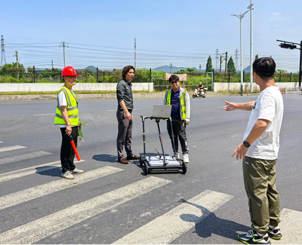 A technician demonstrates ground-penetrating radar equipment operation to staff on the road.