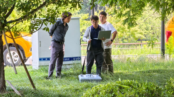 A technician operates ground-penetrating radar equipment on an outdoor grassy field for underground exploration.