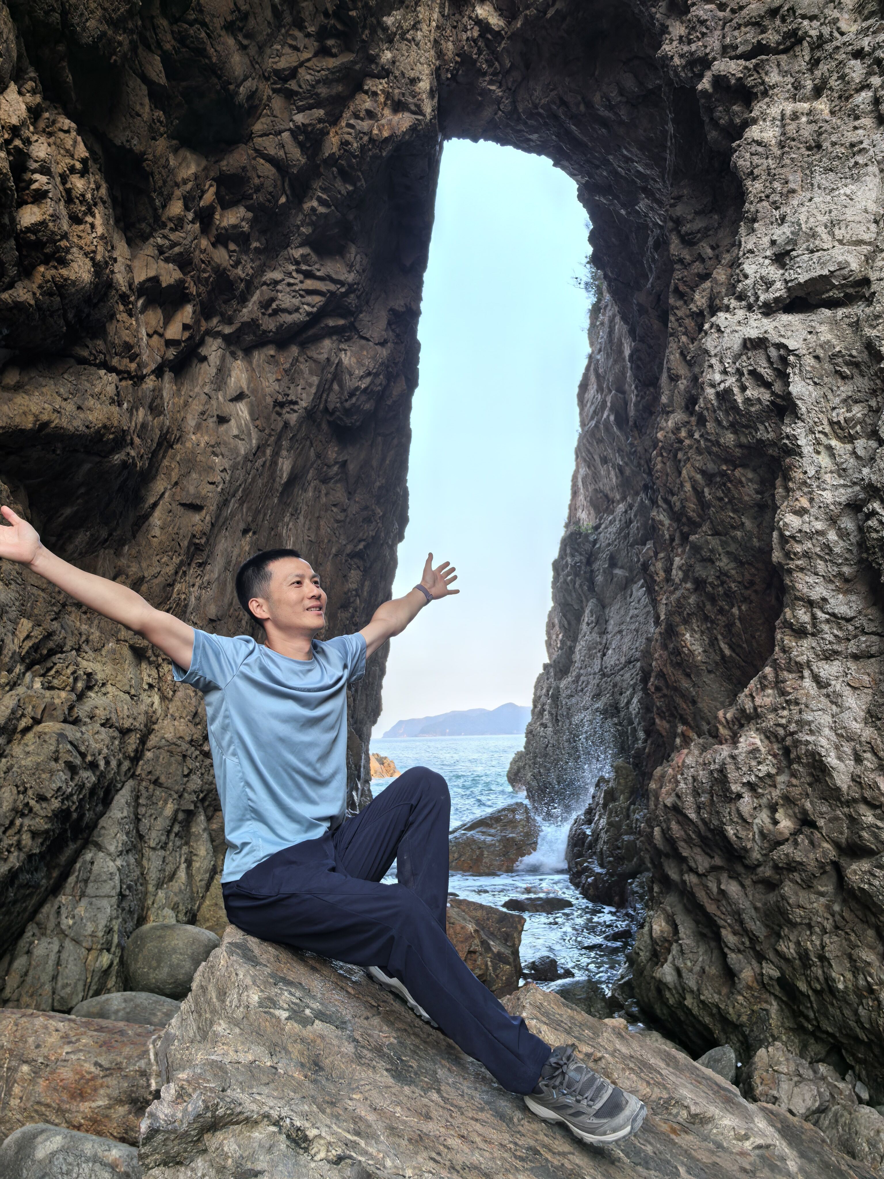 Hiker sitting in rock arch by the sea