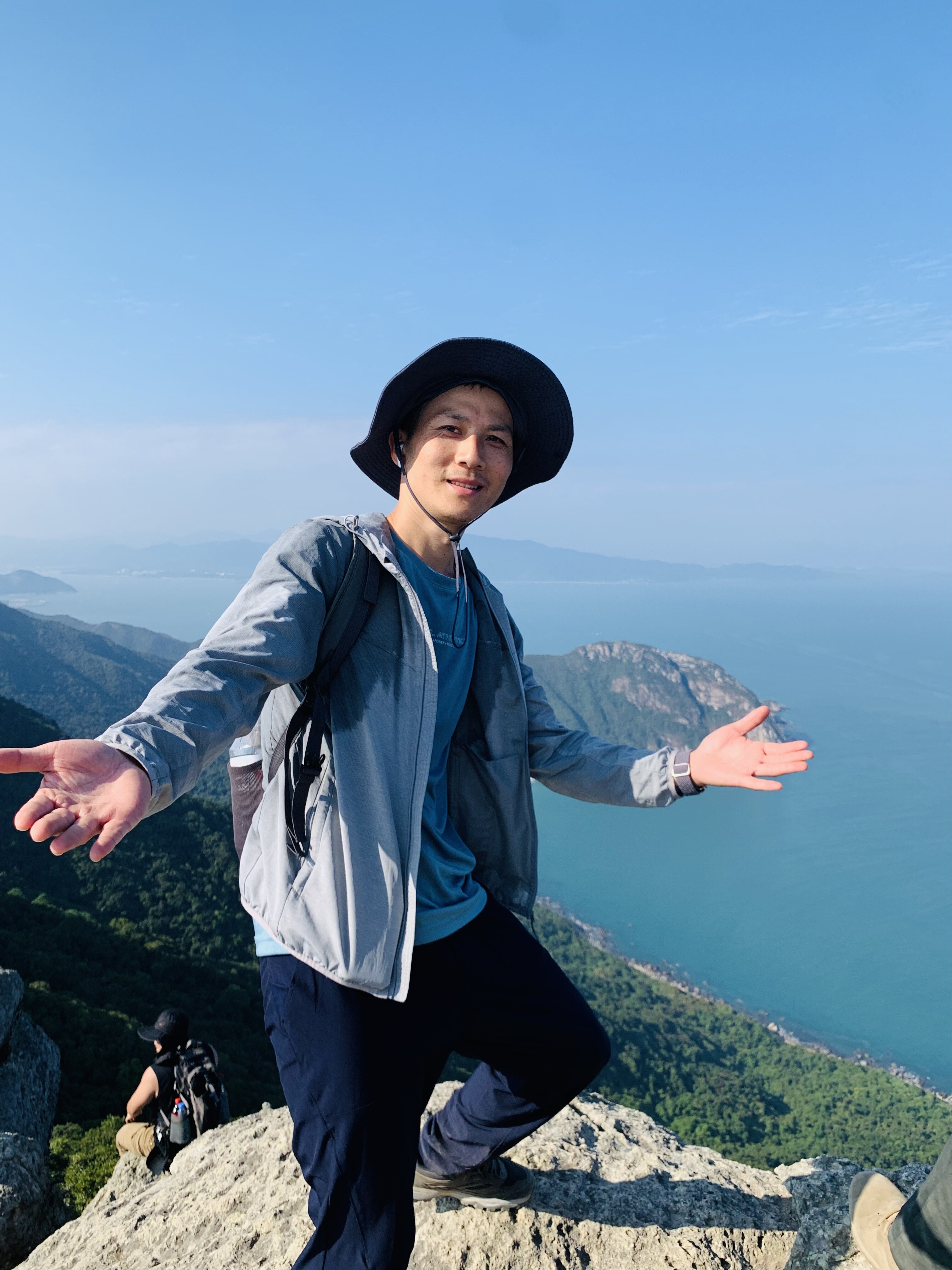 Jacky Liu with arms open on mountain ridge overlooking Shenzhen sea