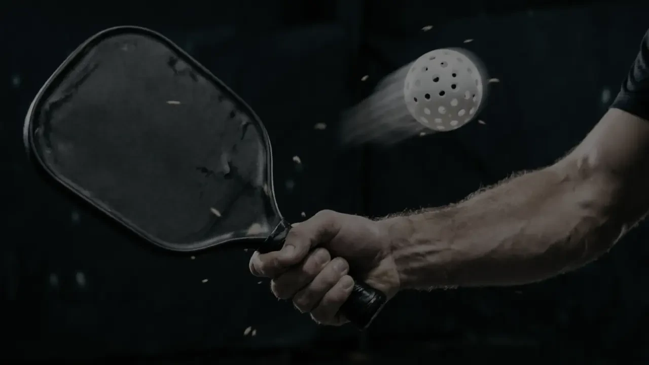Pickleball paddle hitting a ball in a dark studio