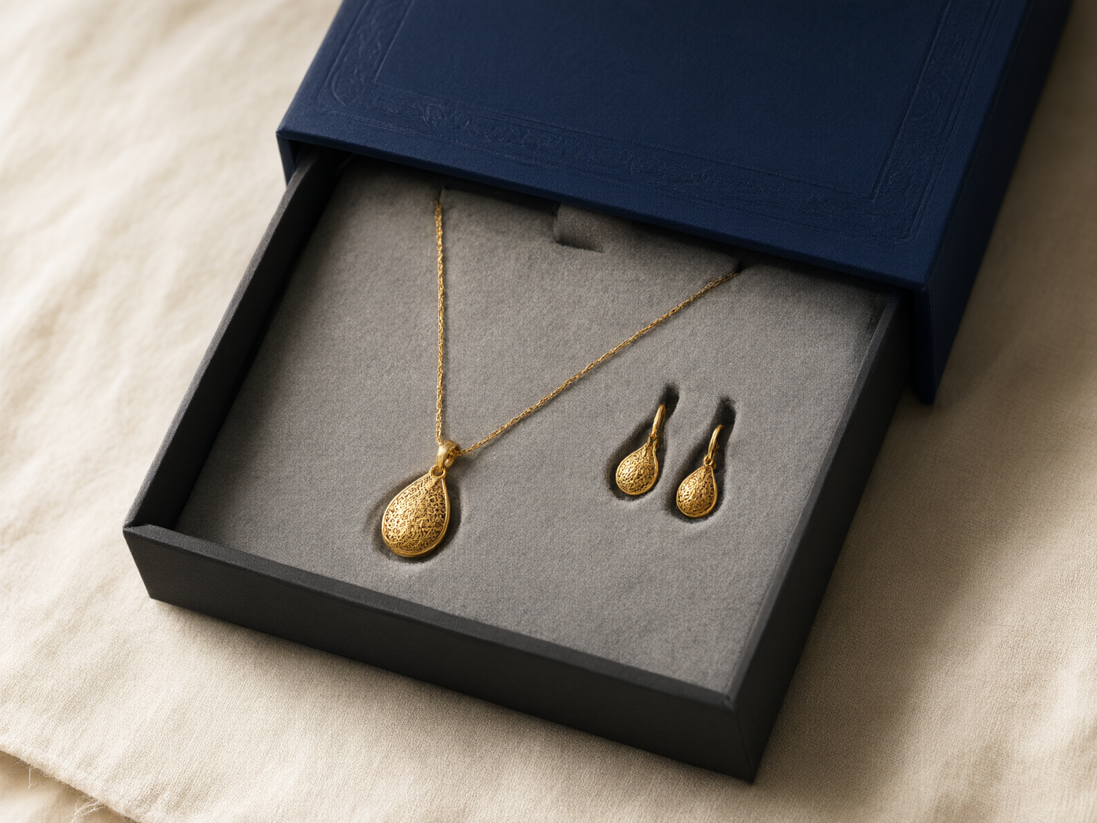 Navy blue drawer box opened to reveal a grey flocked insert holding a gold pendant necklace and matching earrings