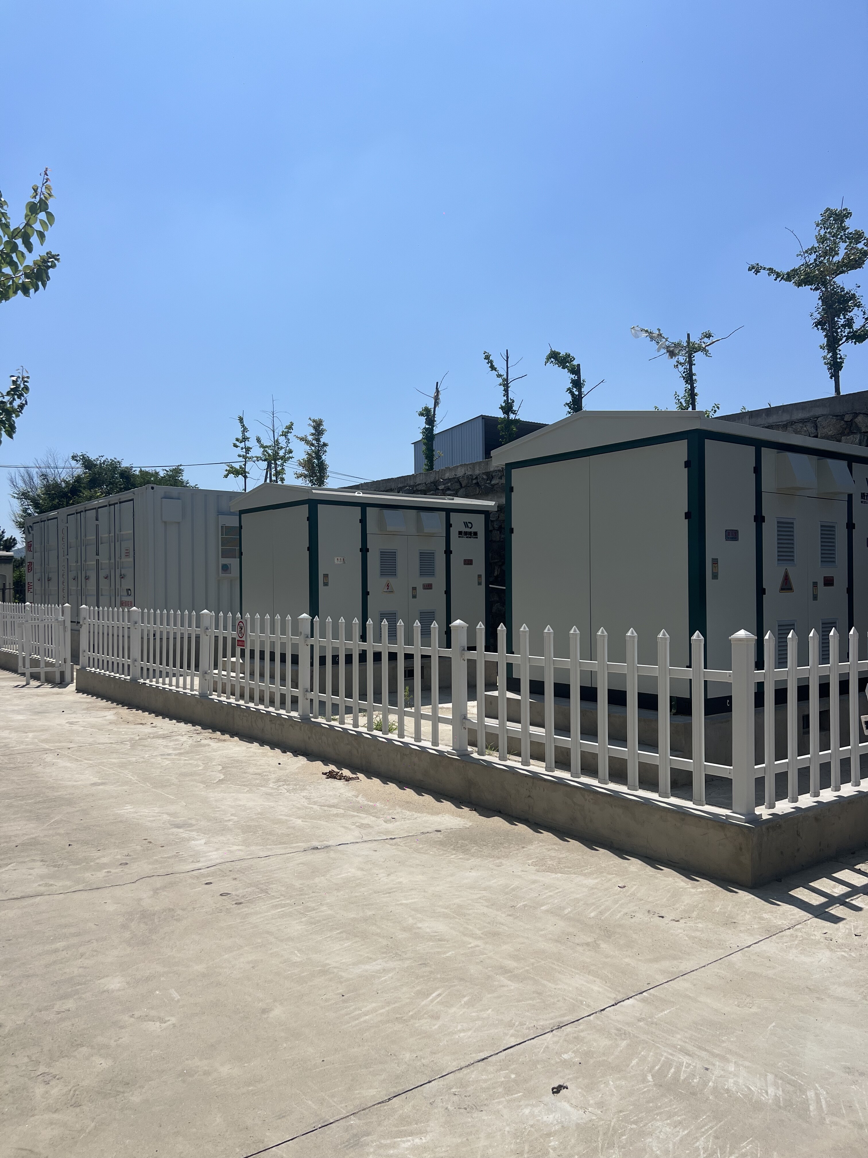 Row of energy storage containers with white fencing in outdoor facility