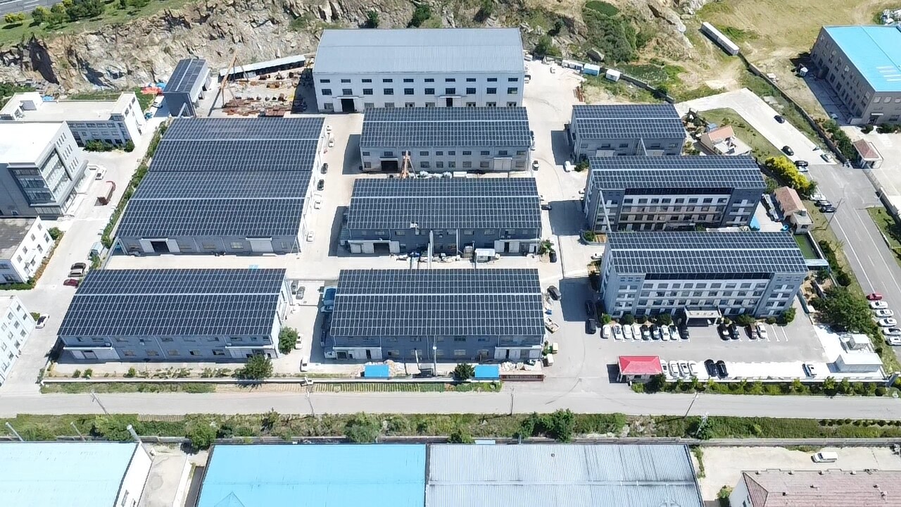 Aerial view of multiple industrial buildings with rooftop solar installations in mountainous area