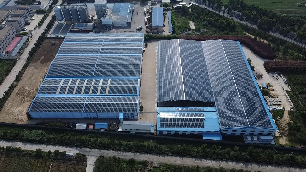 Aerial view of industrial factory buildings with blue roofs covered in solar panel arrays