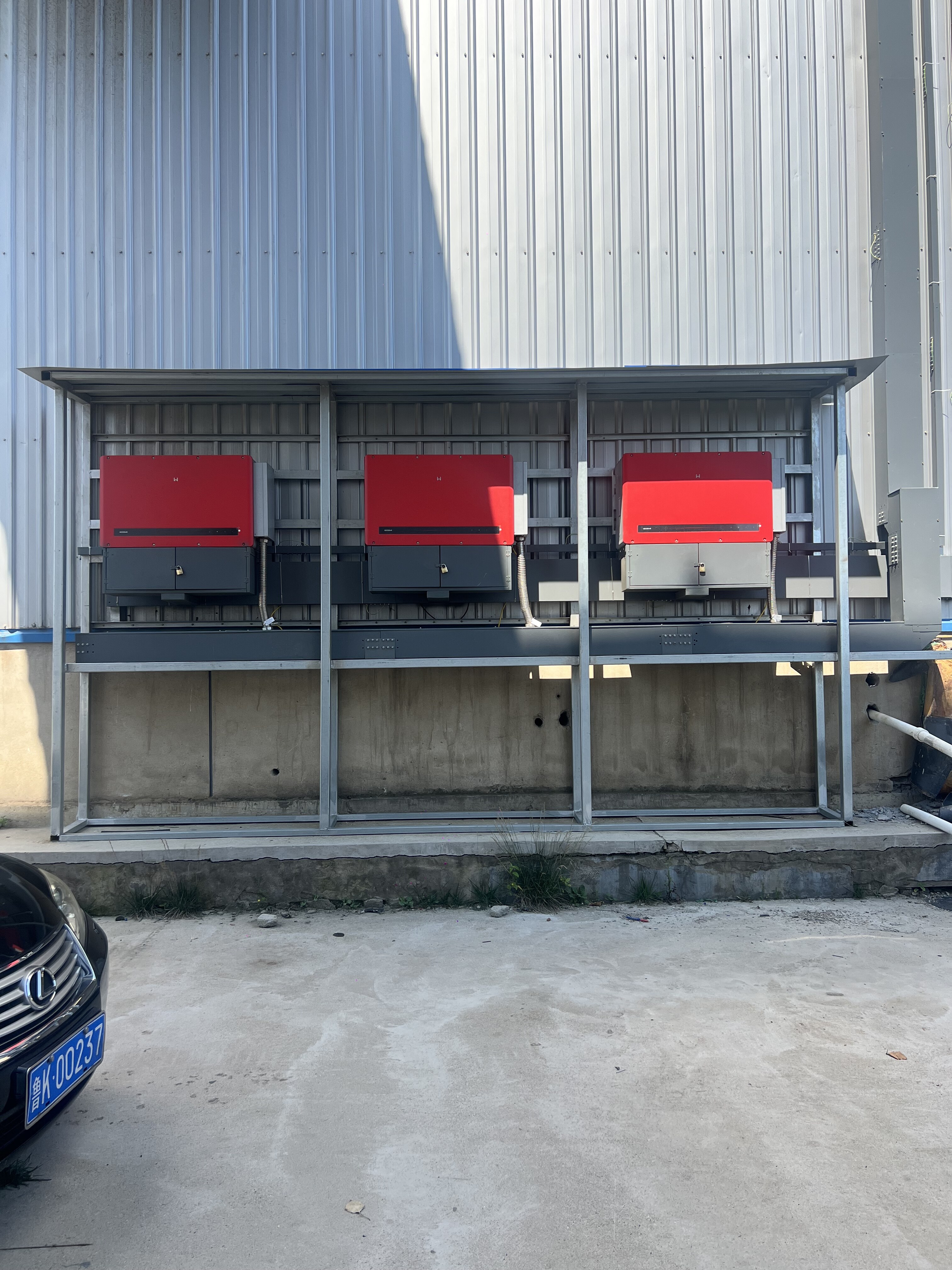 Three red solar inverters mounted on metal frame structure against industrial building wall
