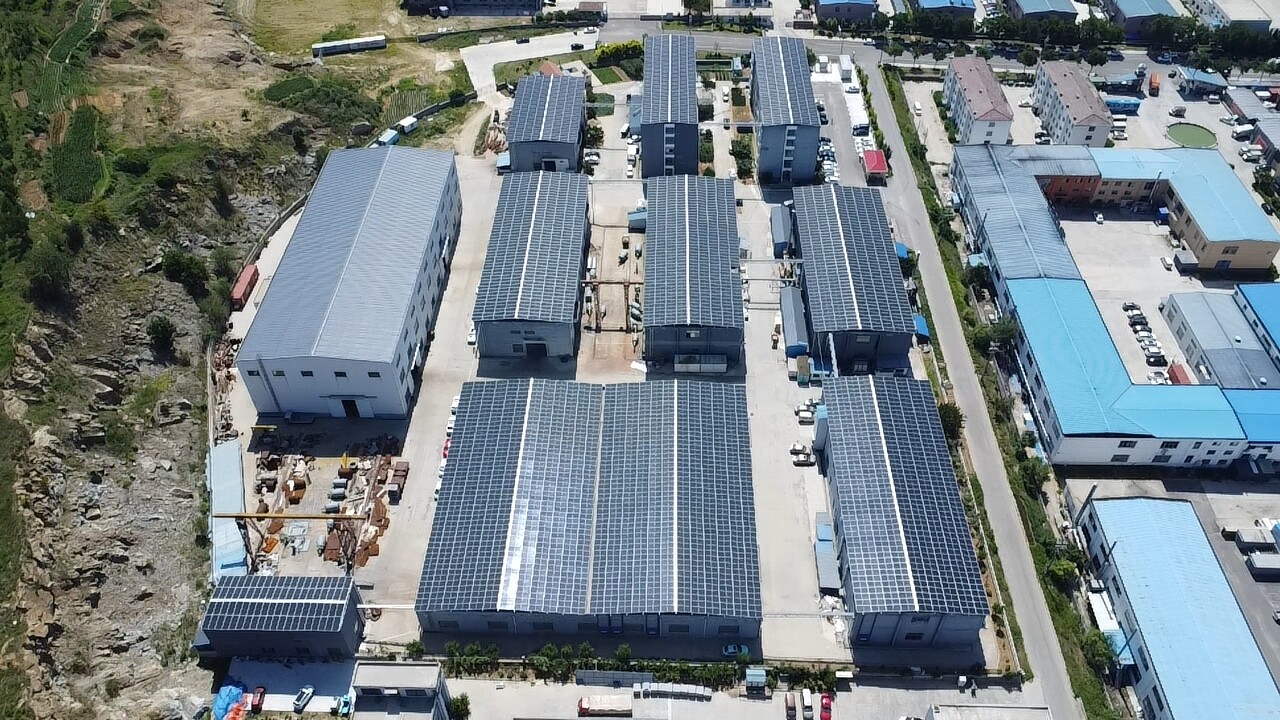 Aerial view of factory complex with solar panels on rooftops near rocky hillside