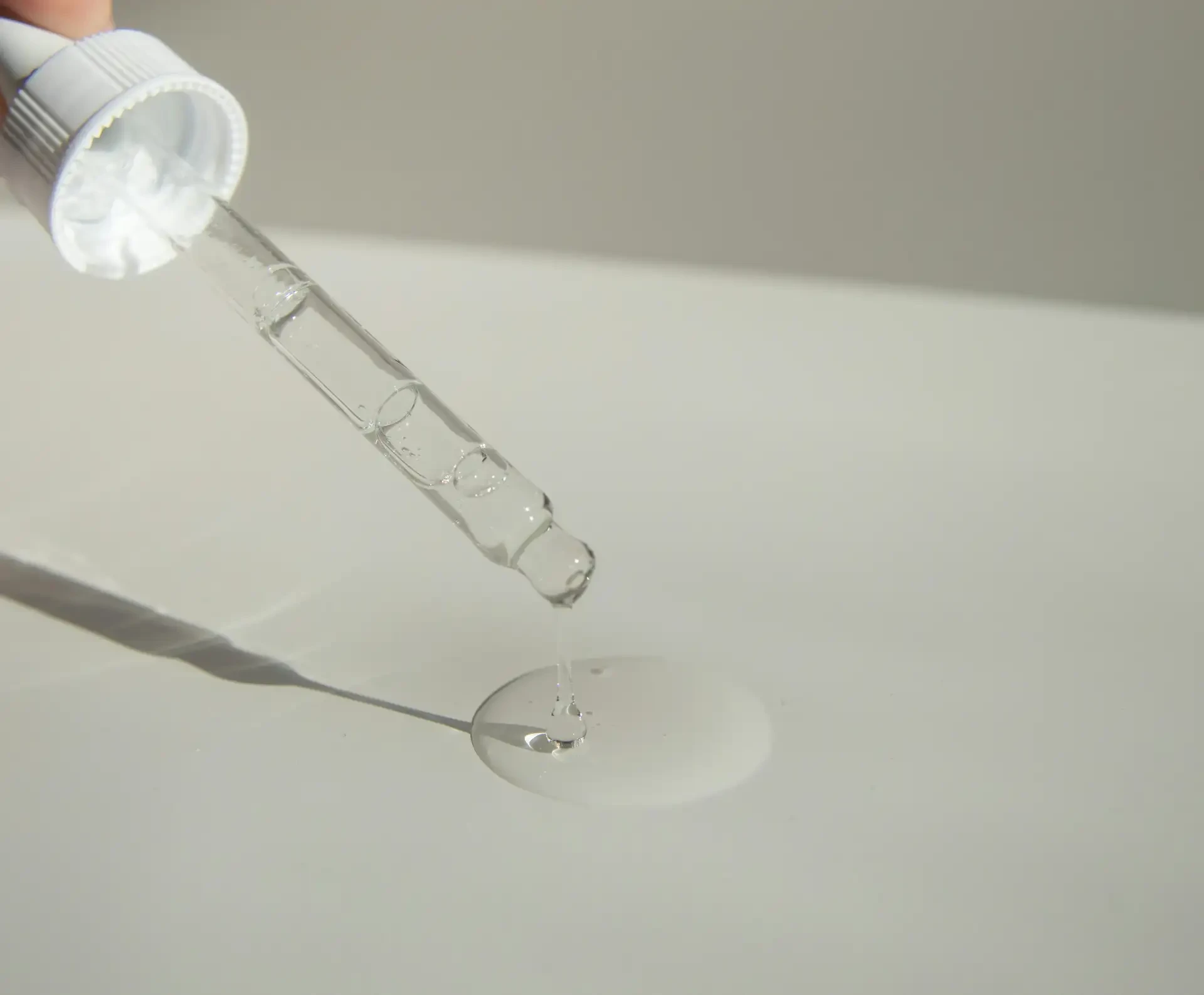 Glass dropper releasing a clear serum droplet onto a smooth surface