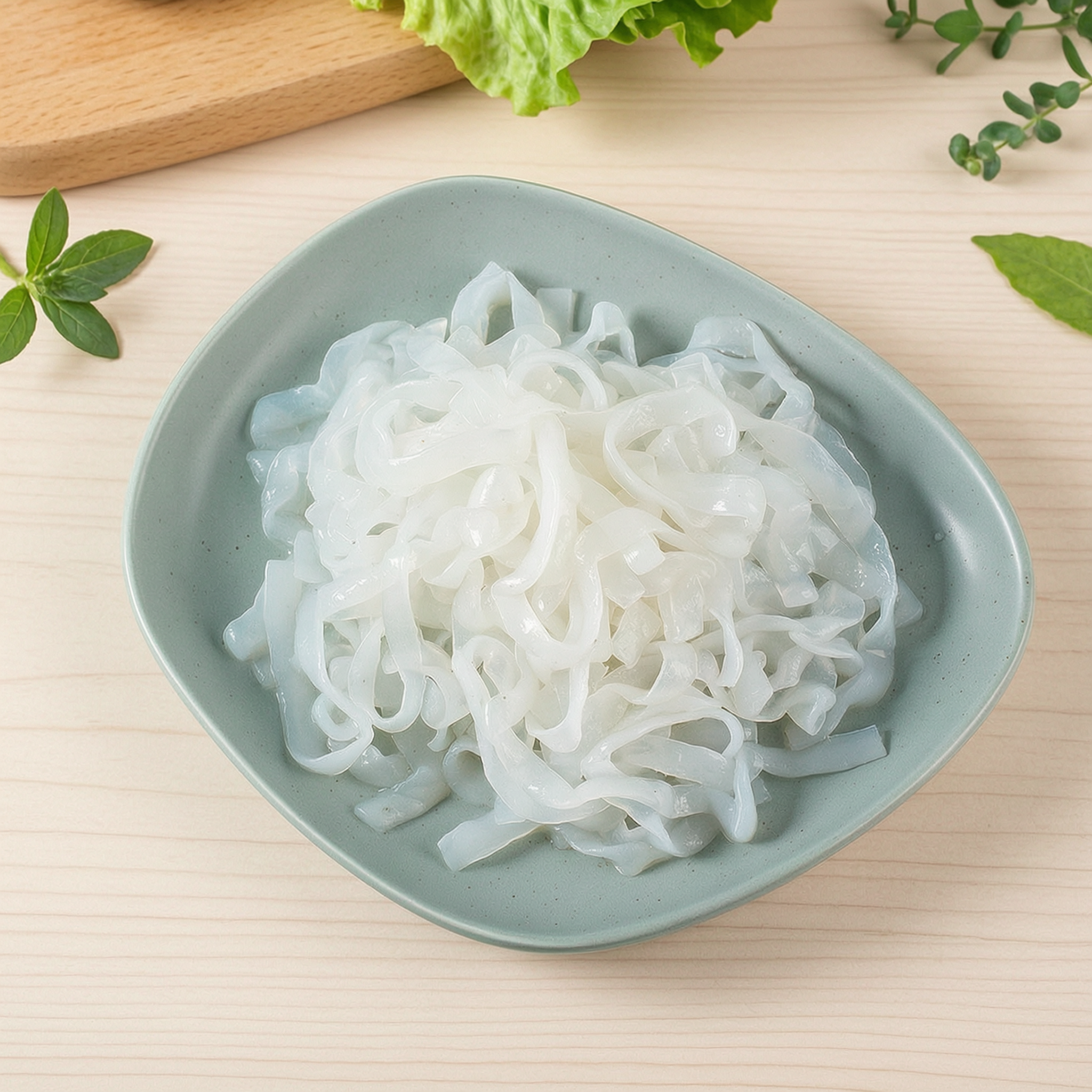 Konjac noodles on a white plate garnished with fresh green herbs, translucent white noodle strands