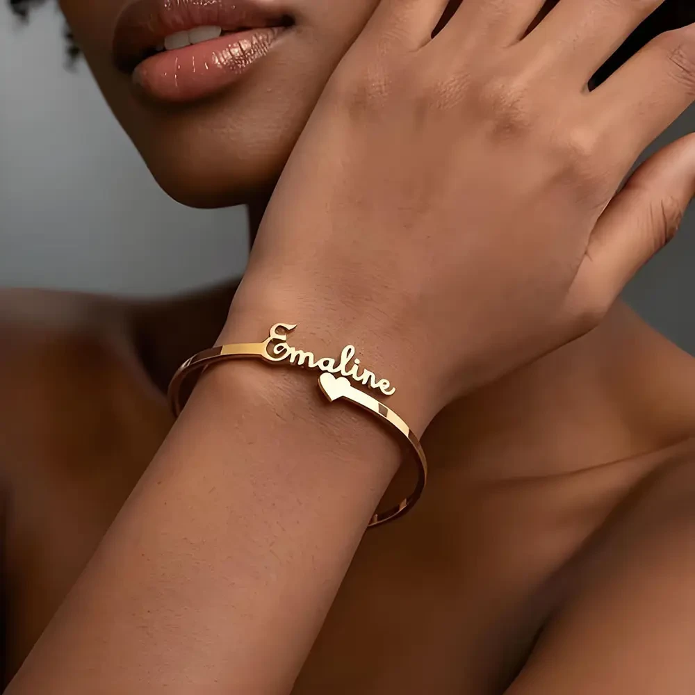 Gold personalized name bangle with heart detail worn on a wrist