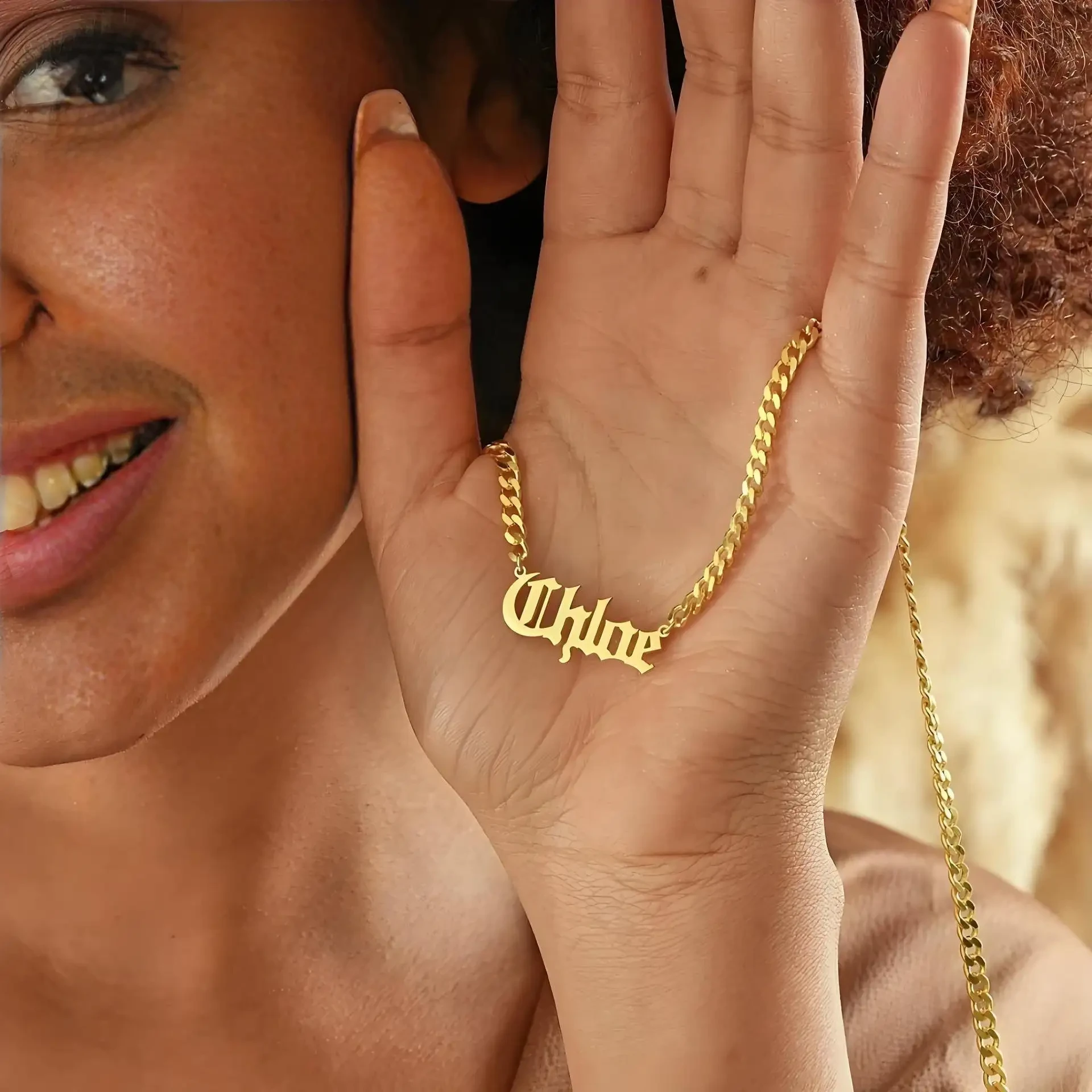 Gold personalized name necklace held in hand against warm natural light