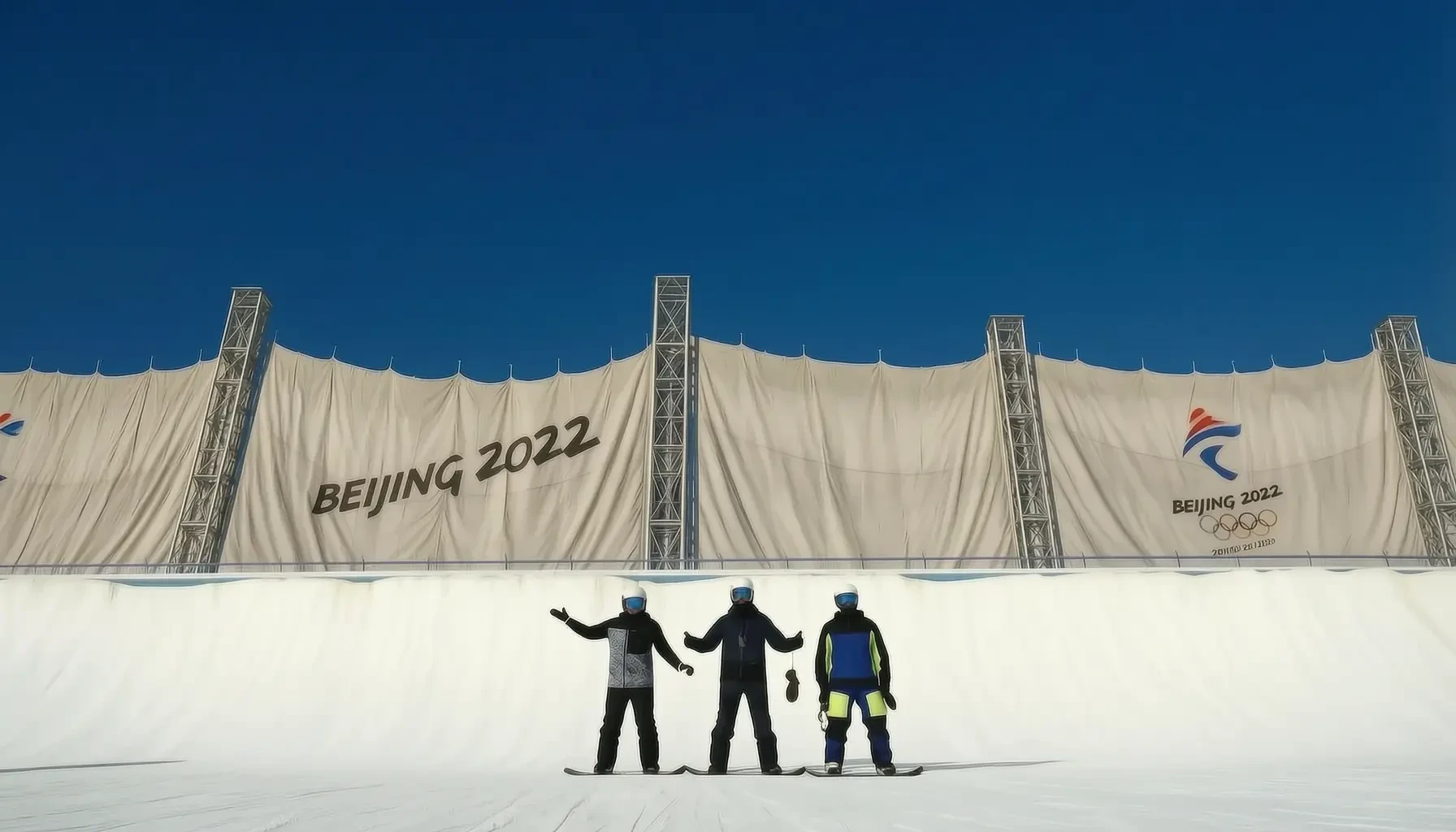 Three snowboarders standing on the snow beneath the Olympic halfpipe banner wall with BEIJING 2022 branding in Chongli