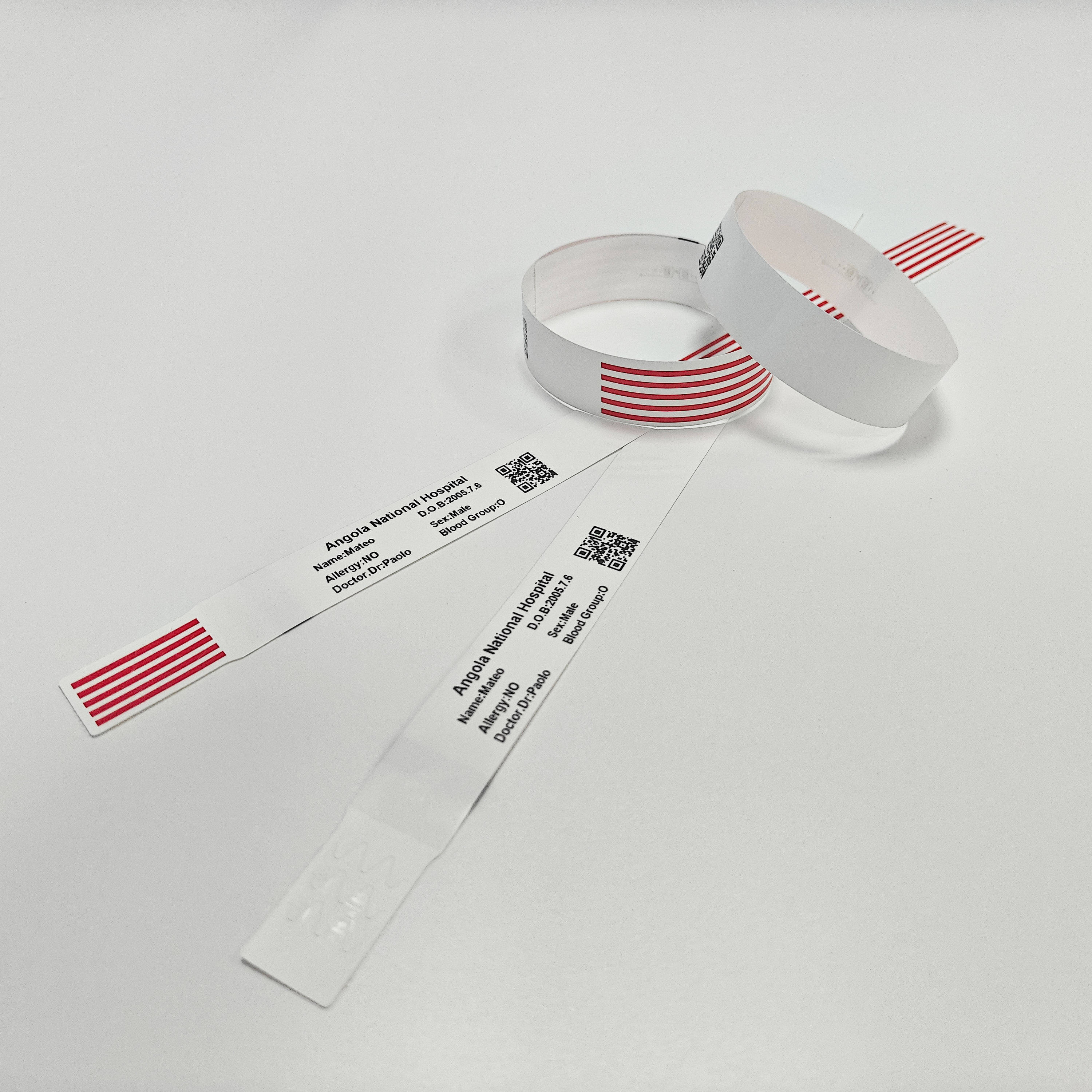 Printed hospital wristbands from Angola National Hospital showing patient information and QR code barcode