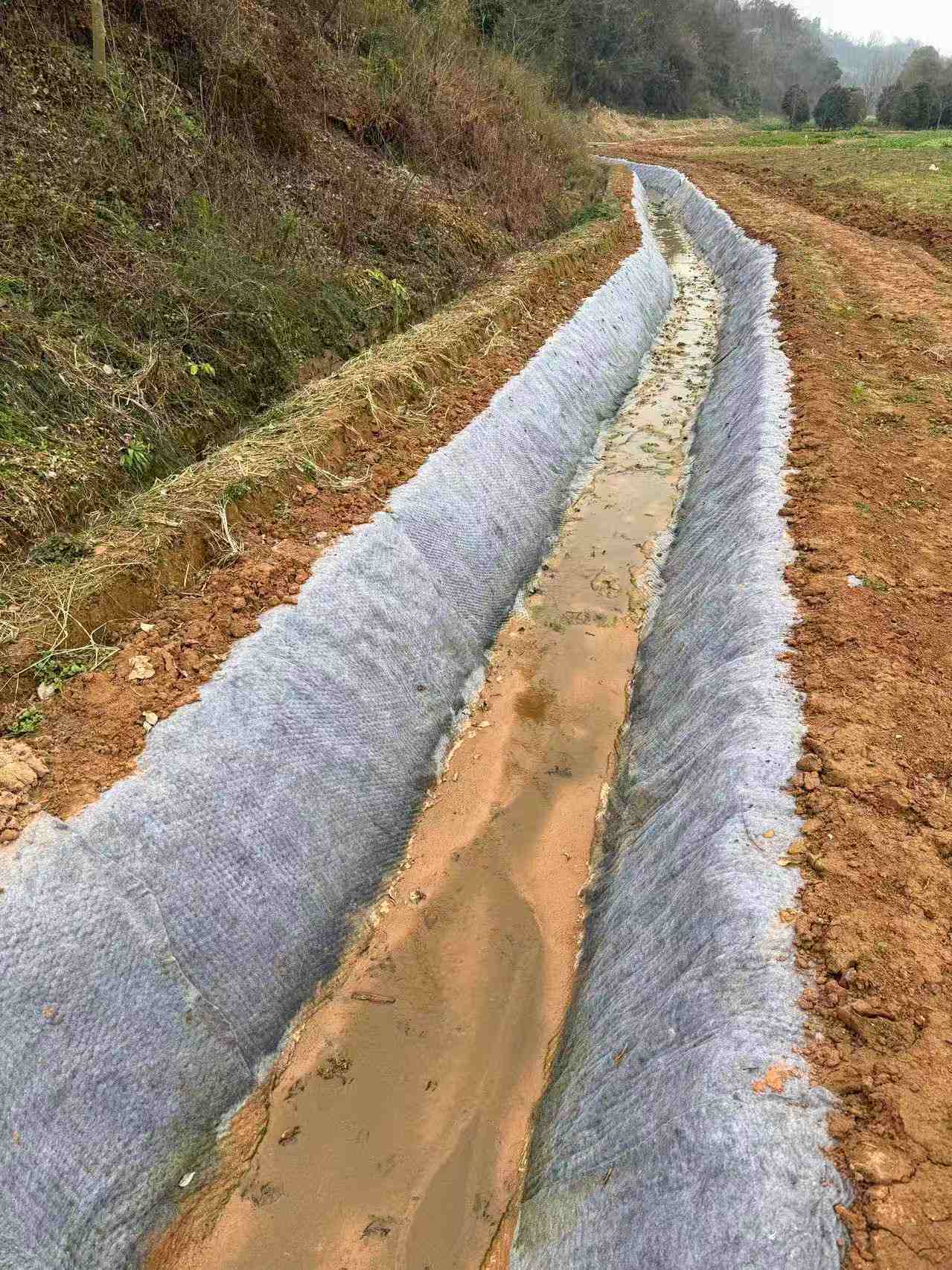 湖北玖坤 JC/T2884 水泥毯随州山体农田排灌渠防渗施工实拍,成型渠道整体无缝阻截渗水