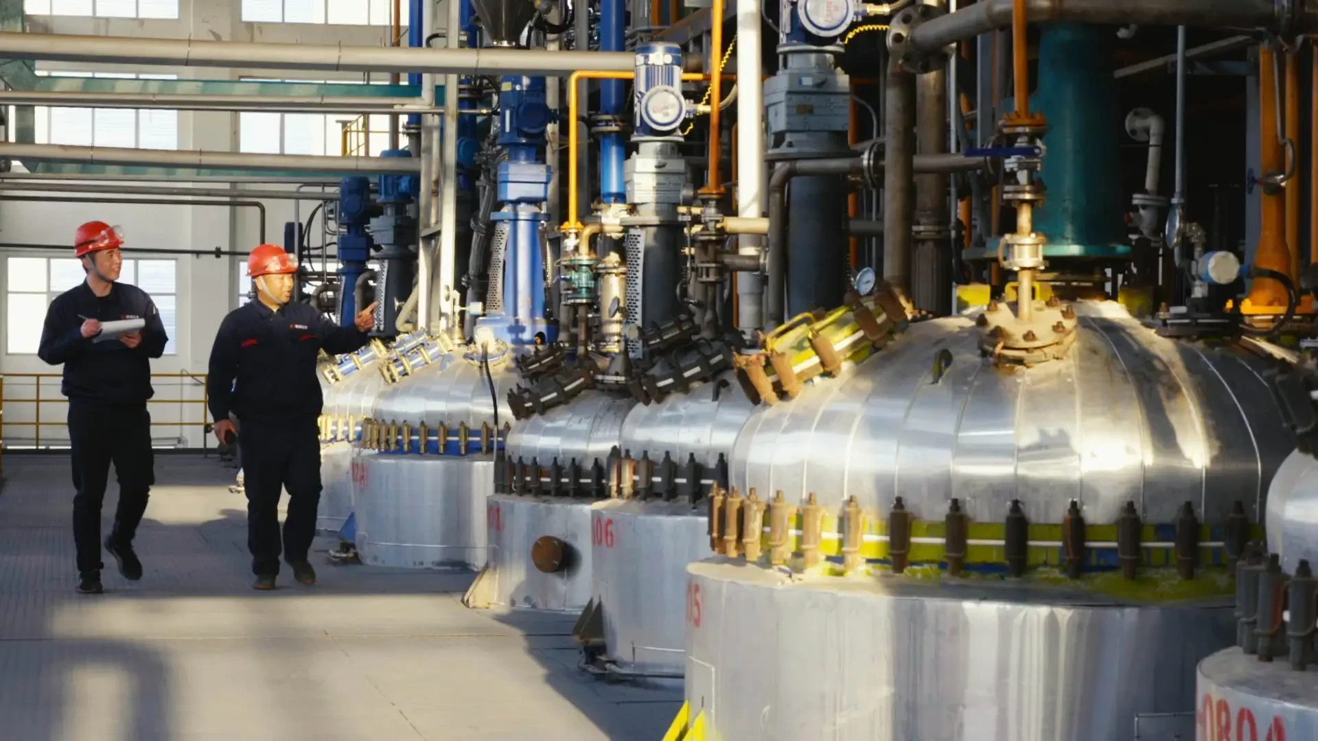 Two process operators walking past reactor vessels inside a chemical plant