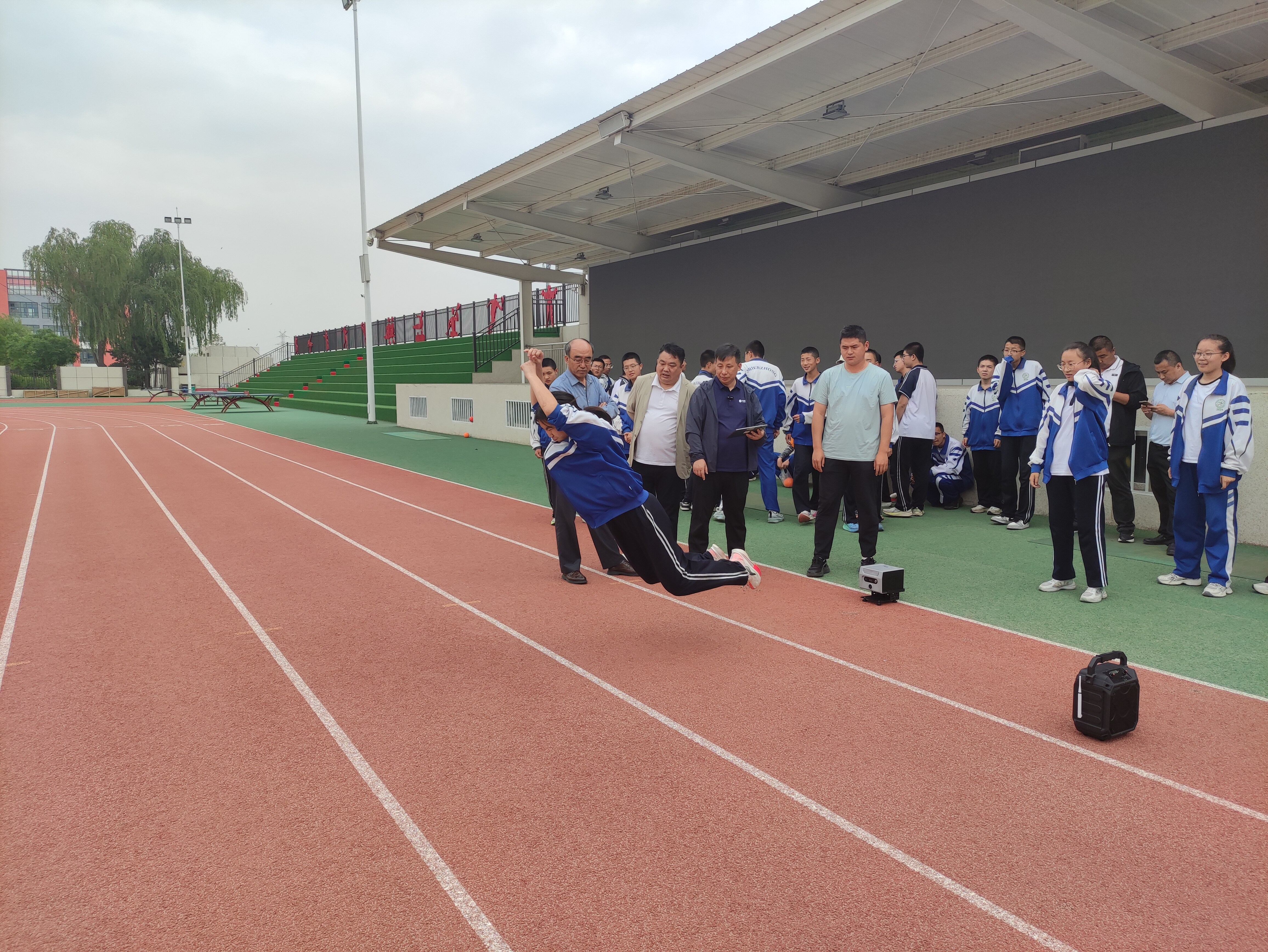 学生在跑道上进行立定跳远腾空动作，体测仪在旁边实时捕捉